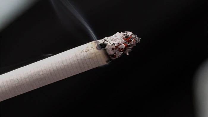 A lit cigarette smoldering and emitting smoke